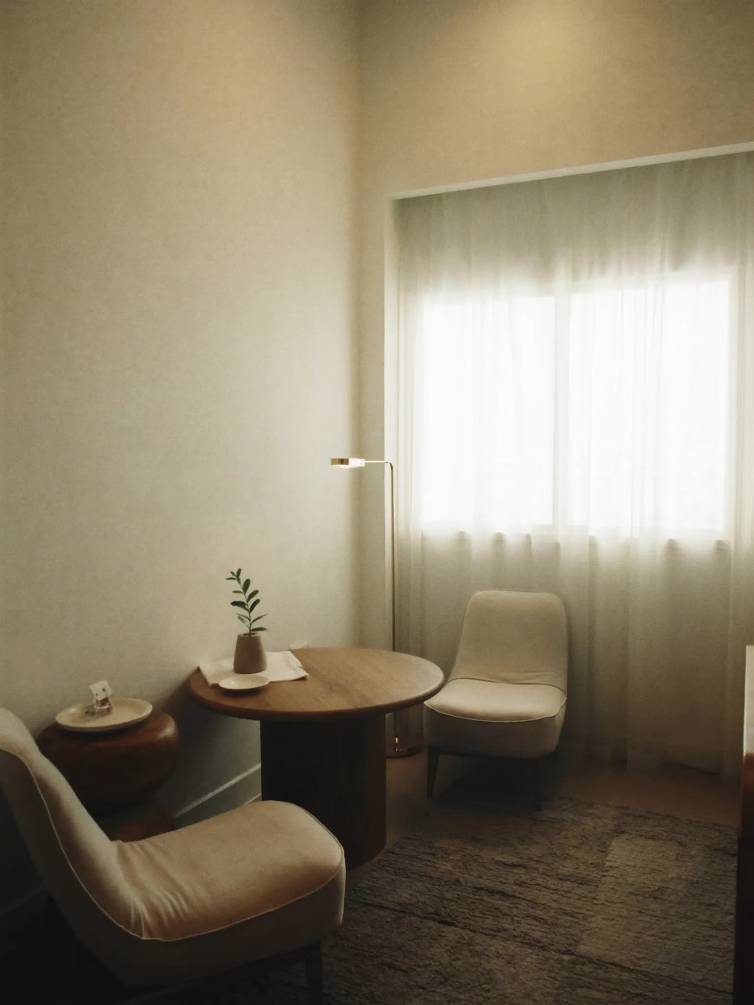 The consultation room at Ngiti — two linen armchairs at a round walnut table by a curtained window
